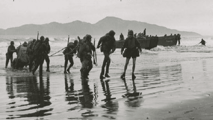 US Marines in World War 2 haul equipment ashore in front of Kāpiti island, with landing craft behind them.