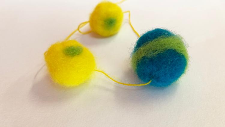 Photo of 2 yellow with green accents felted beads and one blue felted bead with a green accent connected by yellow string. 