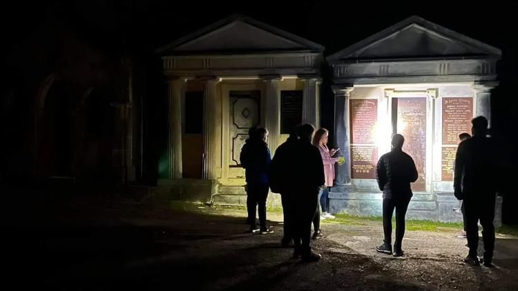 Tour group shining a torch on a crypt in Karori Cemetery at night