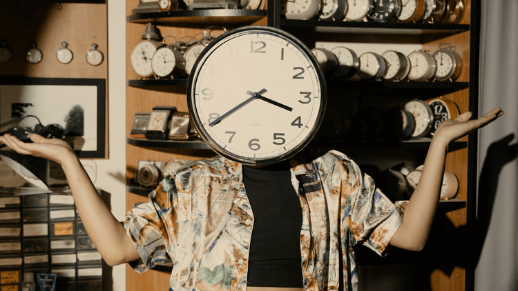 Photo of a person wearing a clock covering their face with a wall lined by shelves filled with clocks.