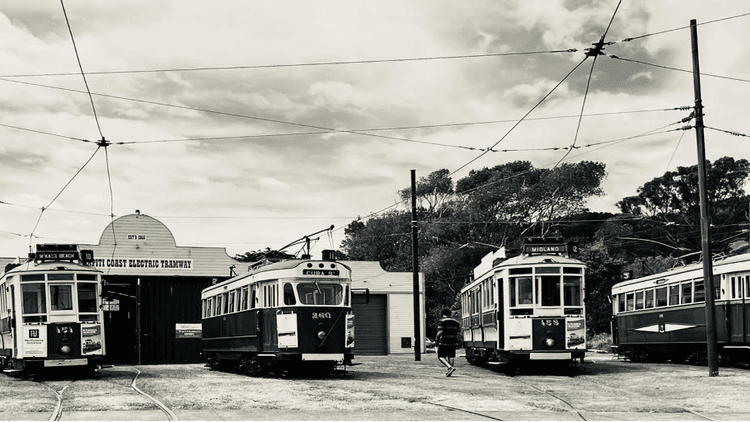 Four historic trams lined up outdoors, black and white