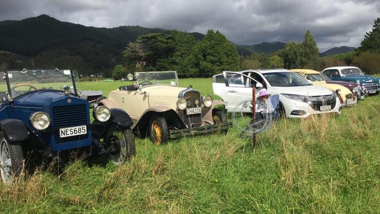 Photo of a mixture of vintage vehicles and one modern vehicle in a field. 